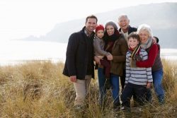 Multi Generation Family In Sand Dunes On Winter Beach Smiling To Camera