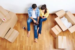 a young couple sitting down in their new home amongst boxes of belongings
